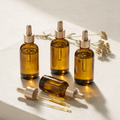 Amber glass Lyquora Glow Oil bottles with champagne droppers and a golden oil bead at the pipette tip