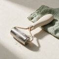 Lyquora IceGlow stainless steel facial ice roller beaded with frost and condensation on bone-white plaster