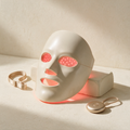 Lyquora LumiGlow LED mask, rigid bone-white contoured shell with red diodes lit and a champagne controller